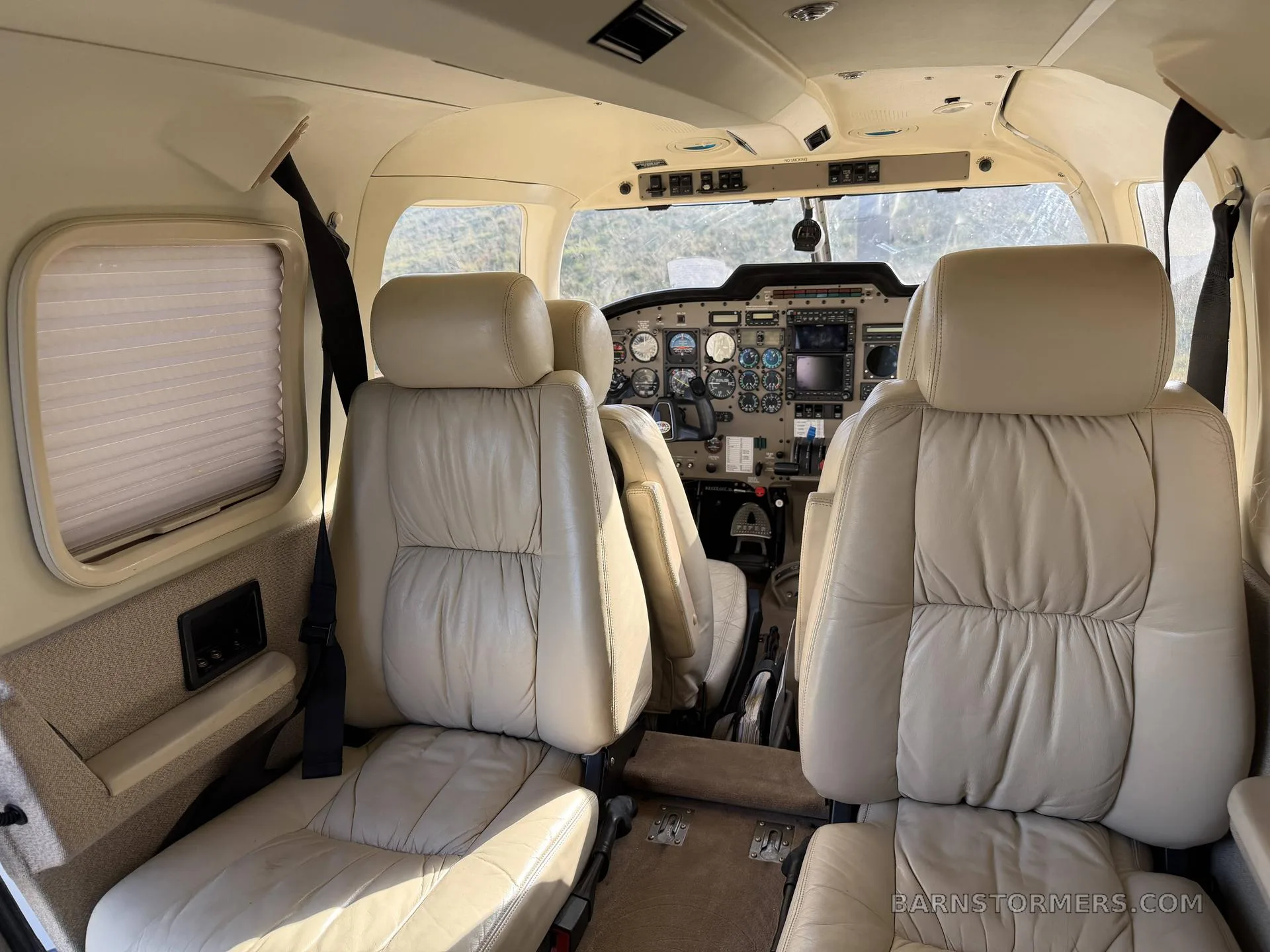 The interior cabin of a Piper Saratoga II TC, featuring light-colored leather seats and a view into the cockpit.