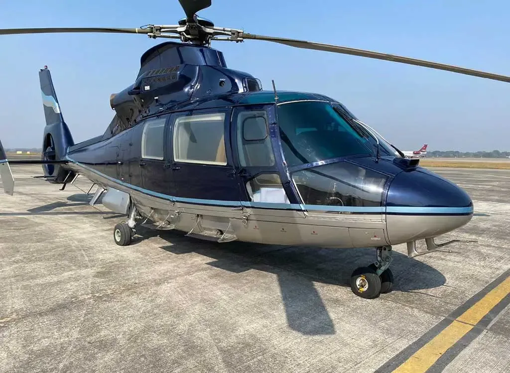 A dark blue and silver Airbus H155 helicopter parked on an asphalt tarmac under a clear sky.