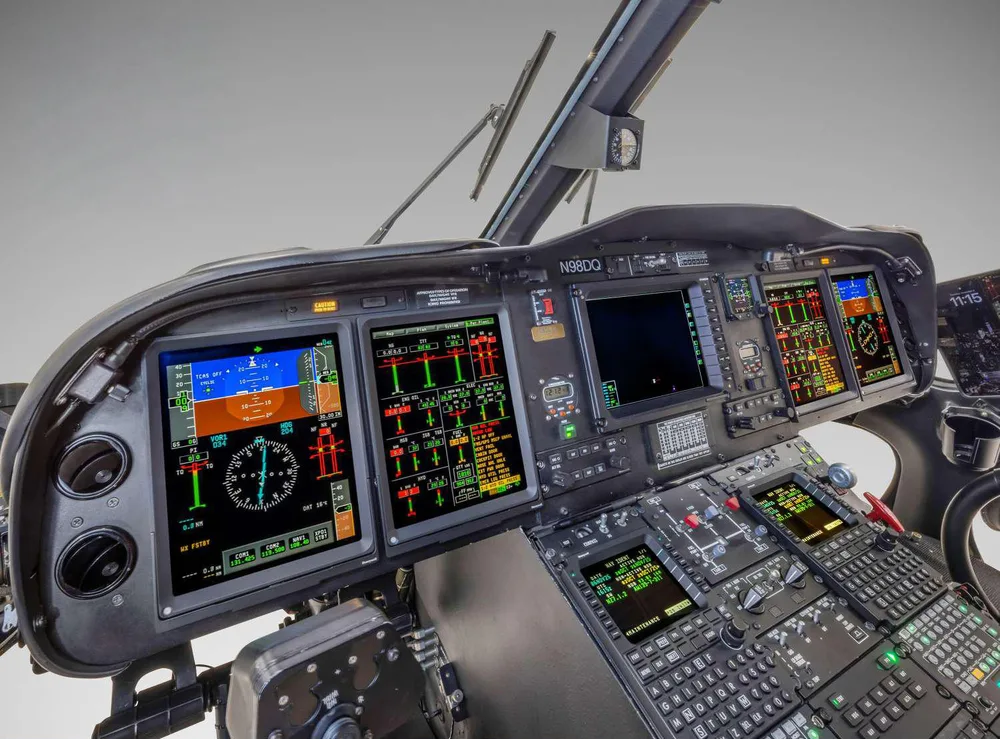 The cockpit of a helicopter with multiple digital displays showing flight data and numerous control panels.