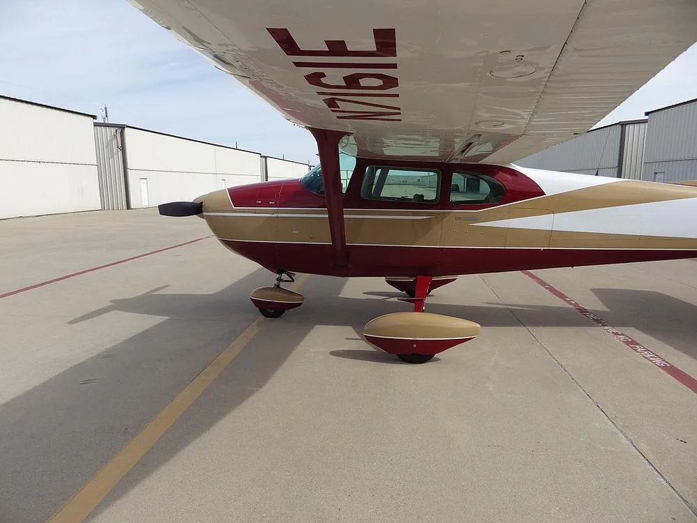 A red, gold, and white high-wing single-engine aircraft with tail number N7161E parked on an airfield tarmac.
