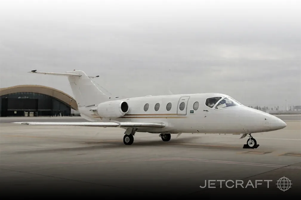 A white business jet with gold stripes parked on a tarmac in front of a hangar.