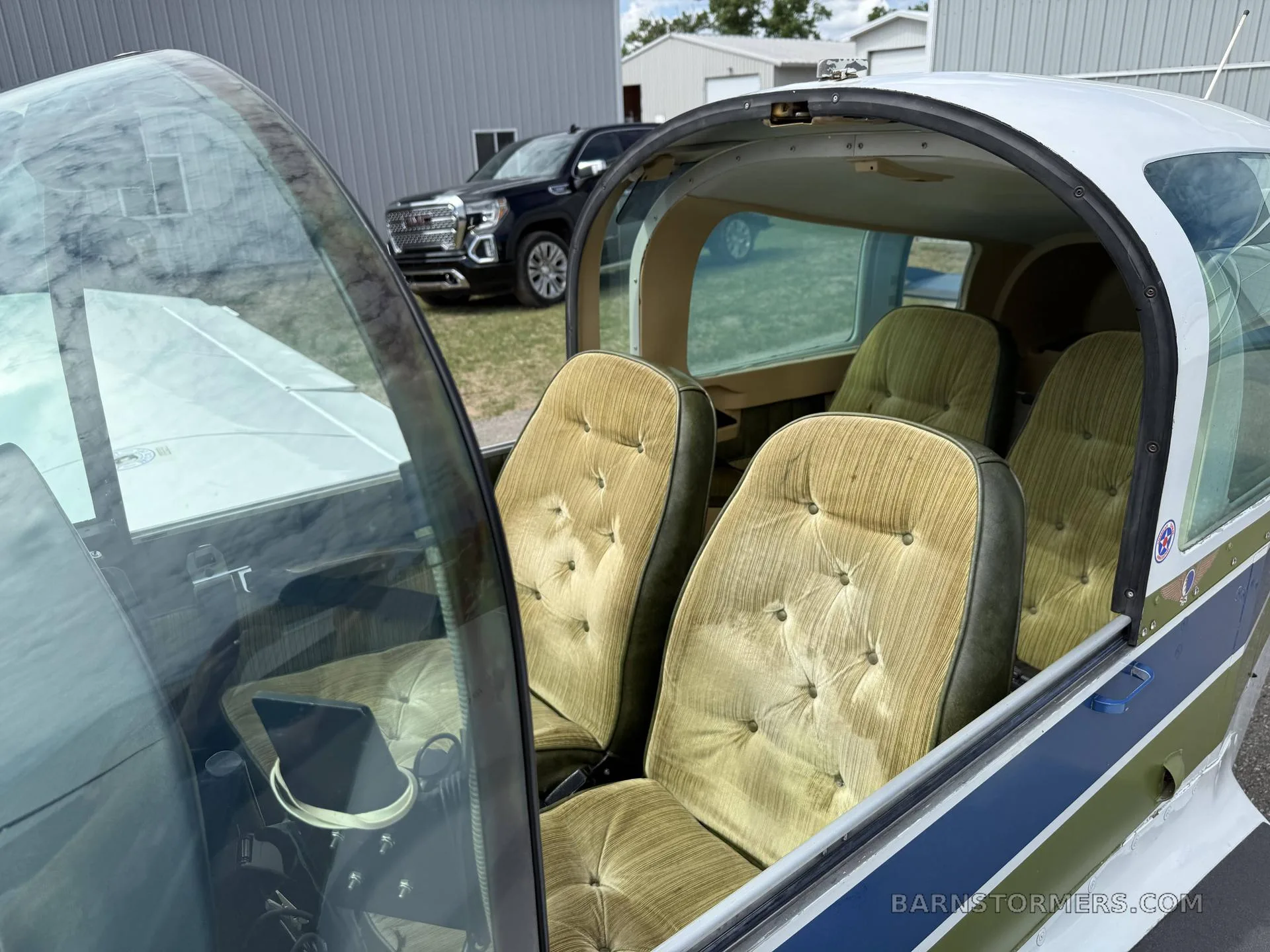 The interior cabin of a Grumman American aircraft, showing four green upholstered seats.