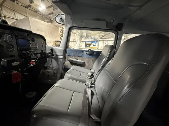The gray interior cabin of a small aircraft, showing two front seats and part of the instrument panel.