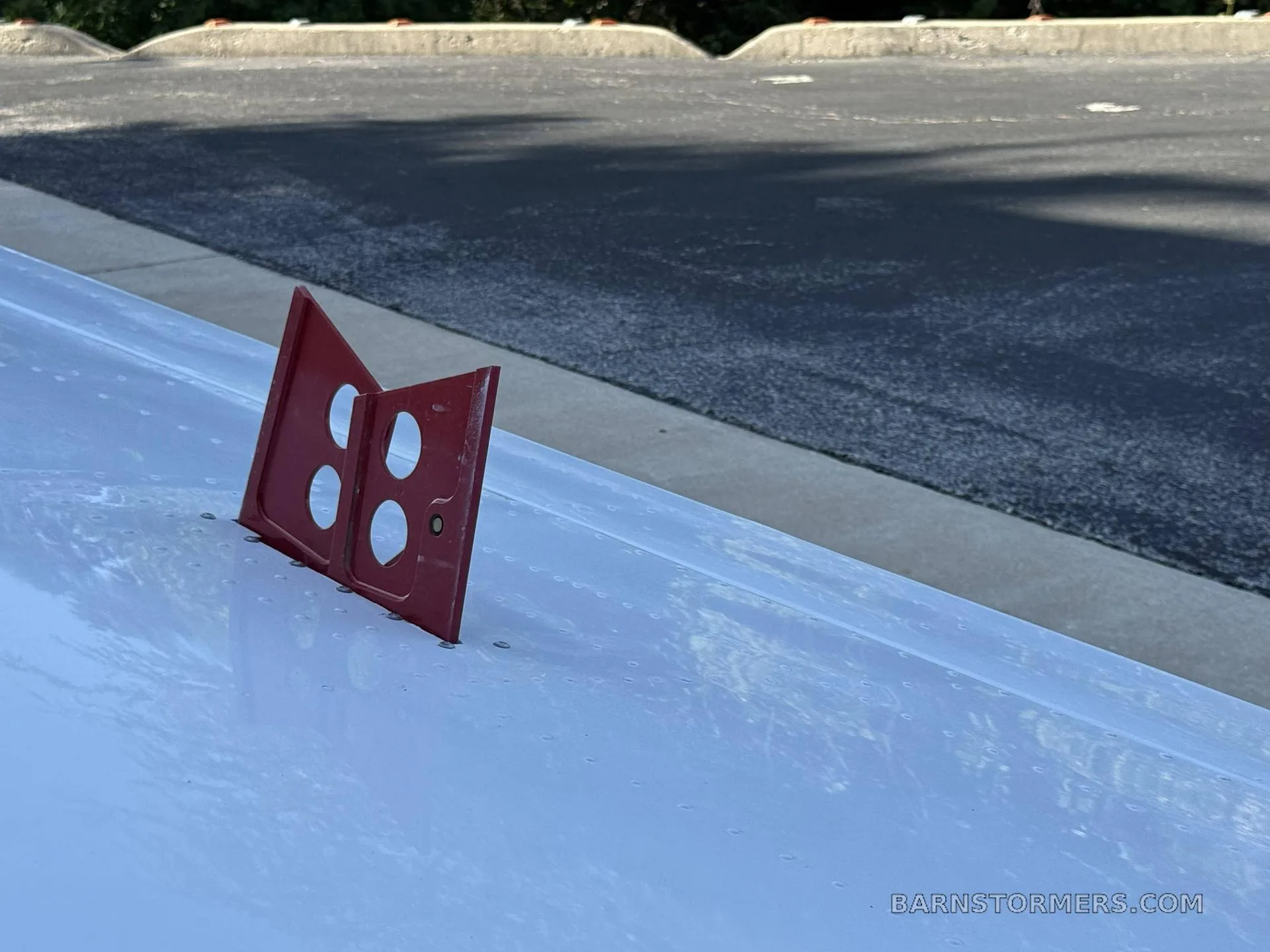 A close-up view of a red vent or fairing on the white surface of an aircraft wing or fuselage.