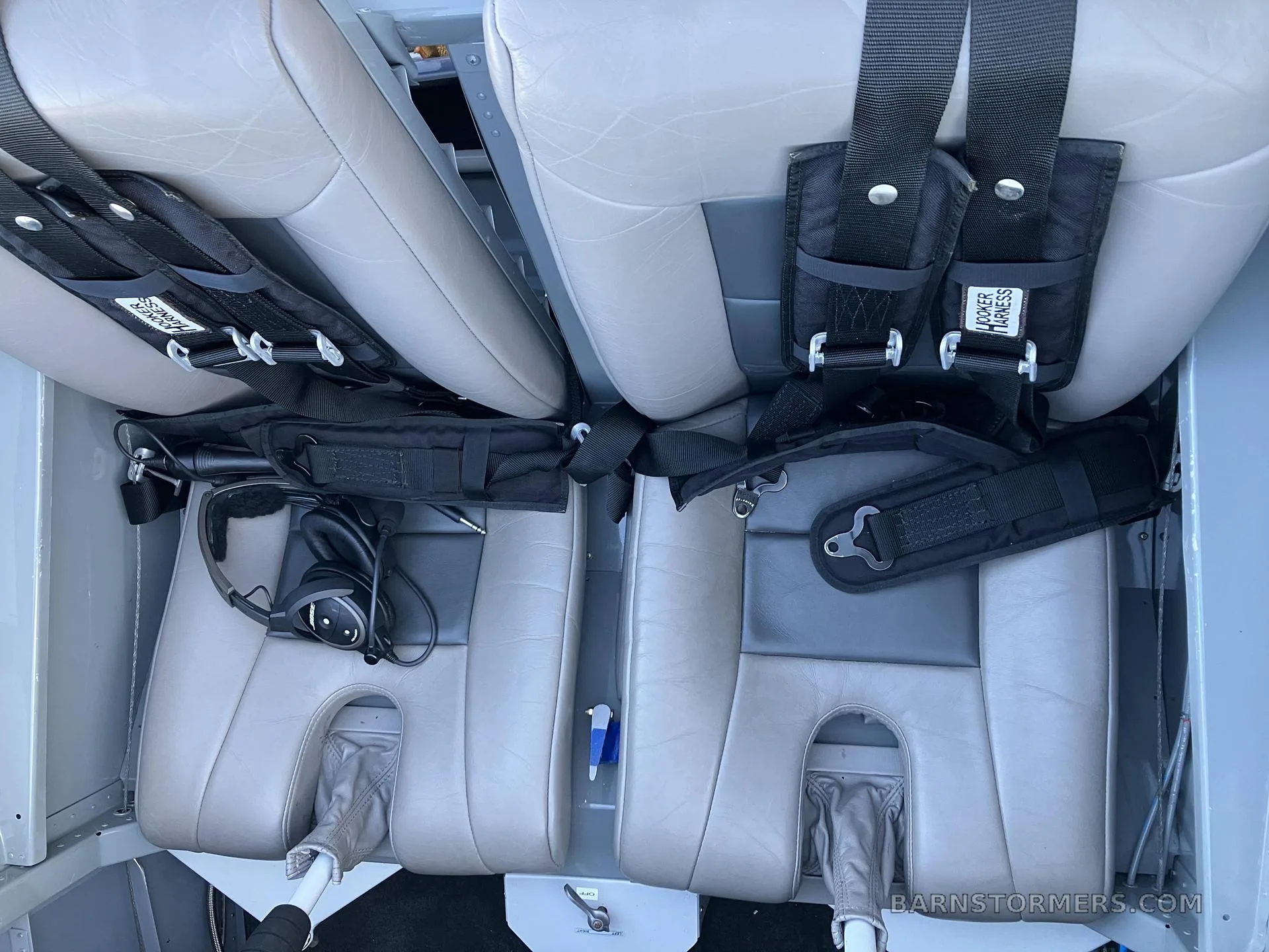Two light grey aircraft seats with black Hooker Harness seatbelts and a headset are visible from above.