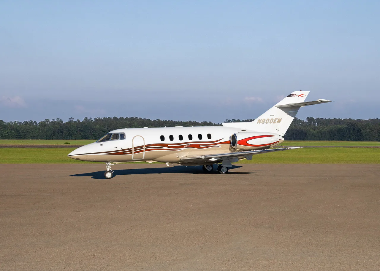 A white and gold business jet with red accents and registration N800EM parked on a tarmac.