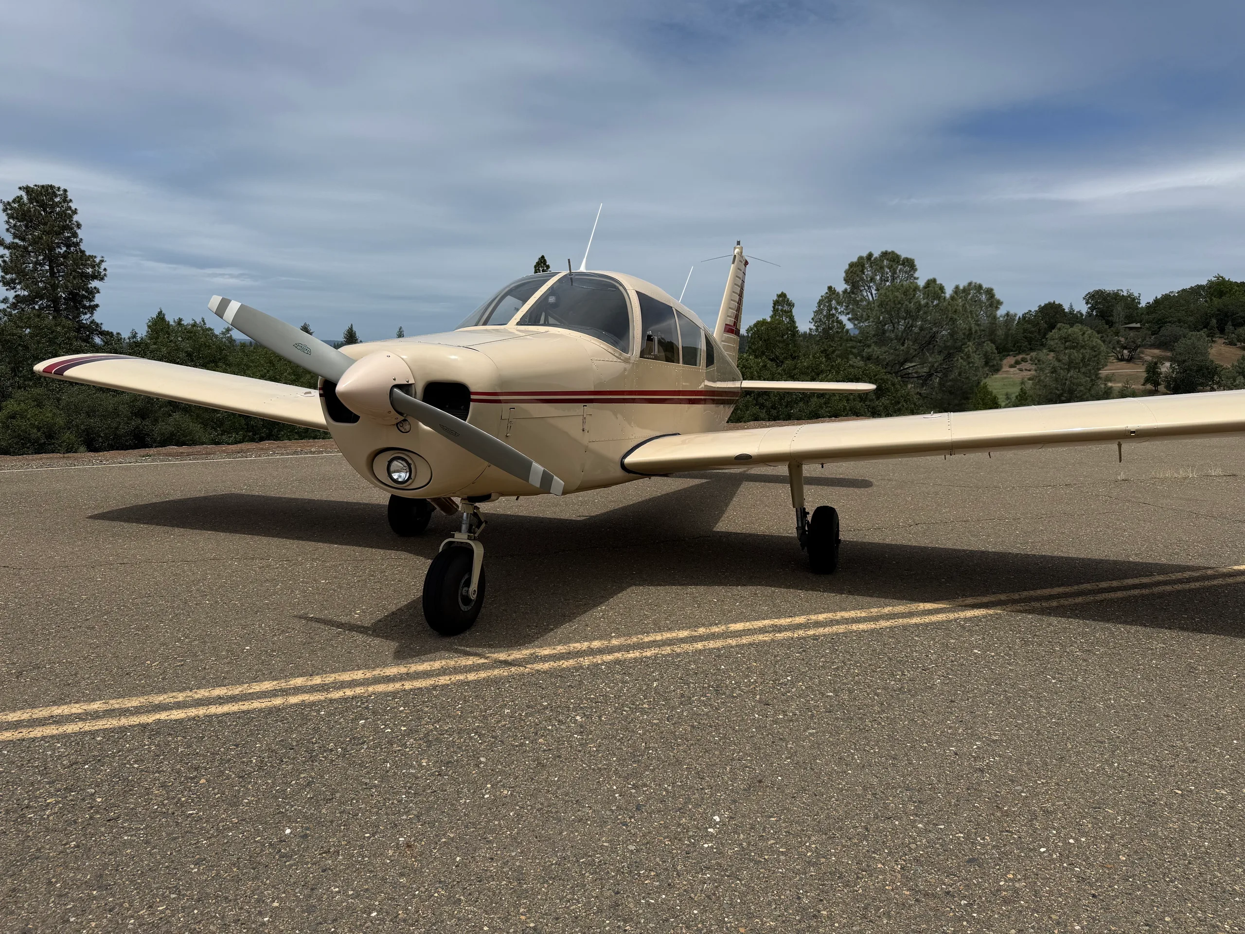 Front view of a cream-colored single-engine aircraft with a red stripe on an asphalt surface.
