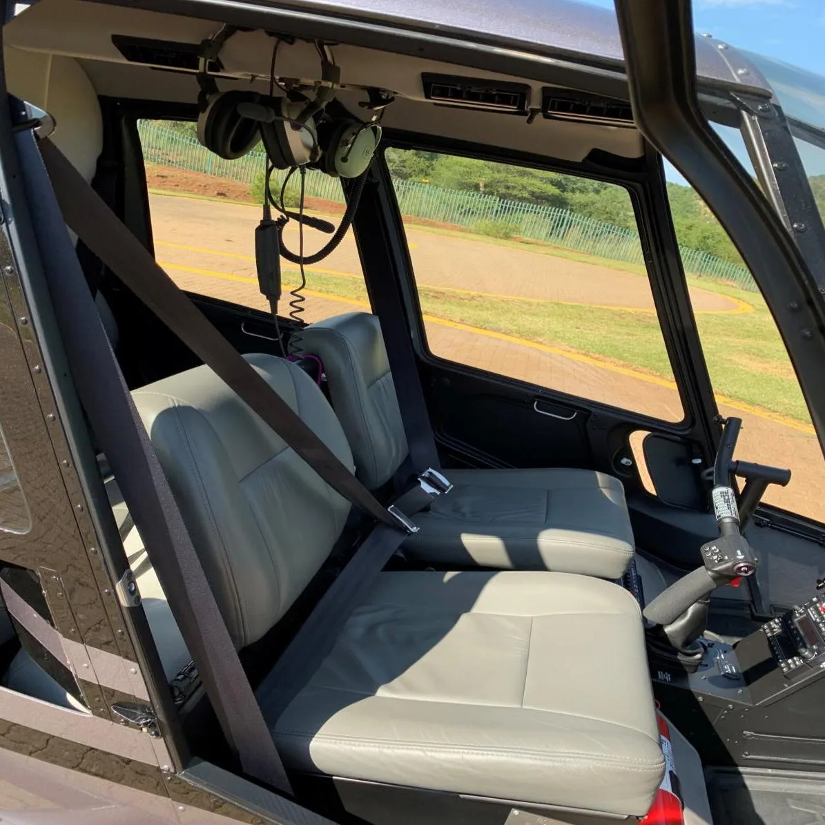 The light grey leather seats and interior of a Robinson R44 helicopter, with headsets hanging above.