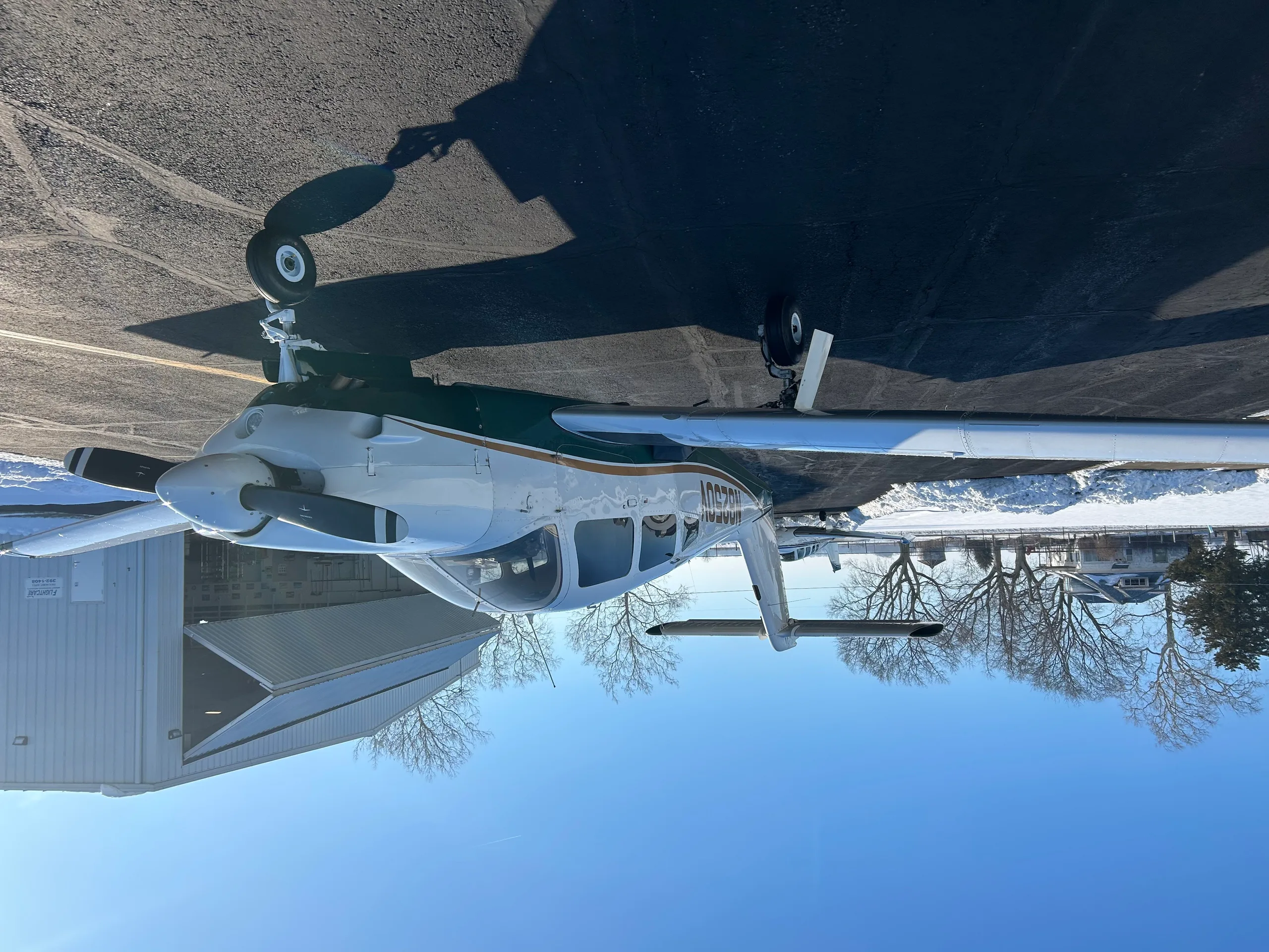 A white and green single-engine aircraft, N8250V, parked on an asphalt ramp with snow on the ground.