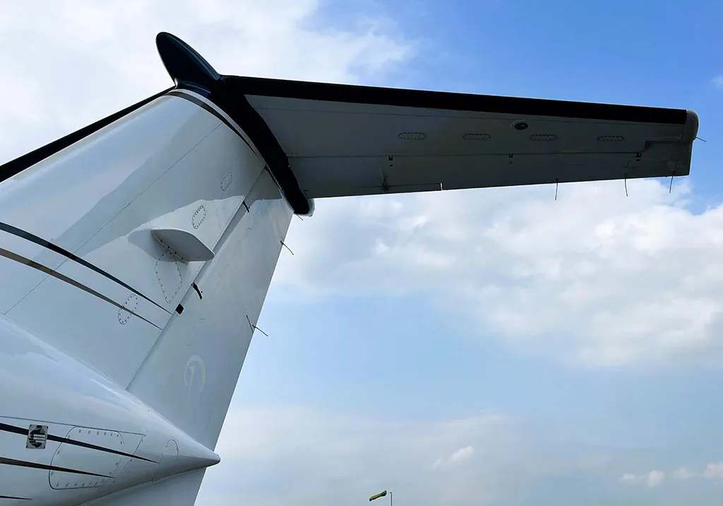 A close-up view of the white tail and horizontal stabilizer of a Beechcraft King Air 250 aircraft against a blue sky.