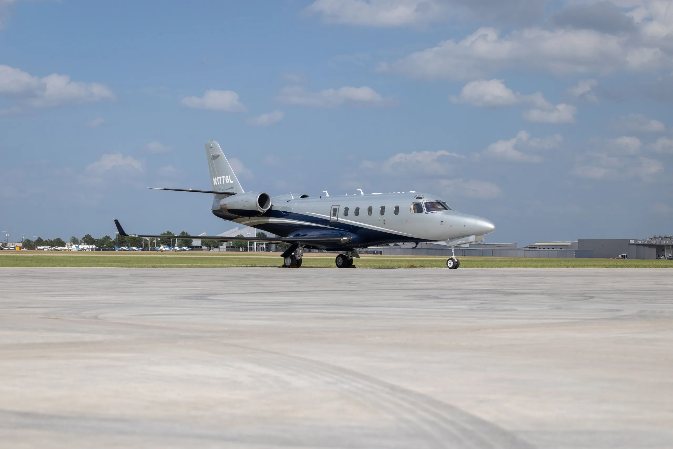 A Learjet 60 in a two-tone grey and dark blue paint scheme, parked on an airport tarmac under a partly cloudy sky.