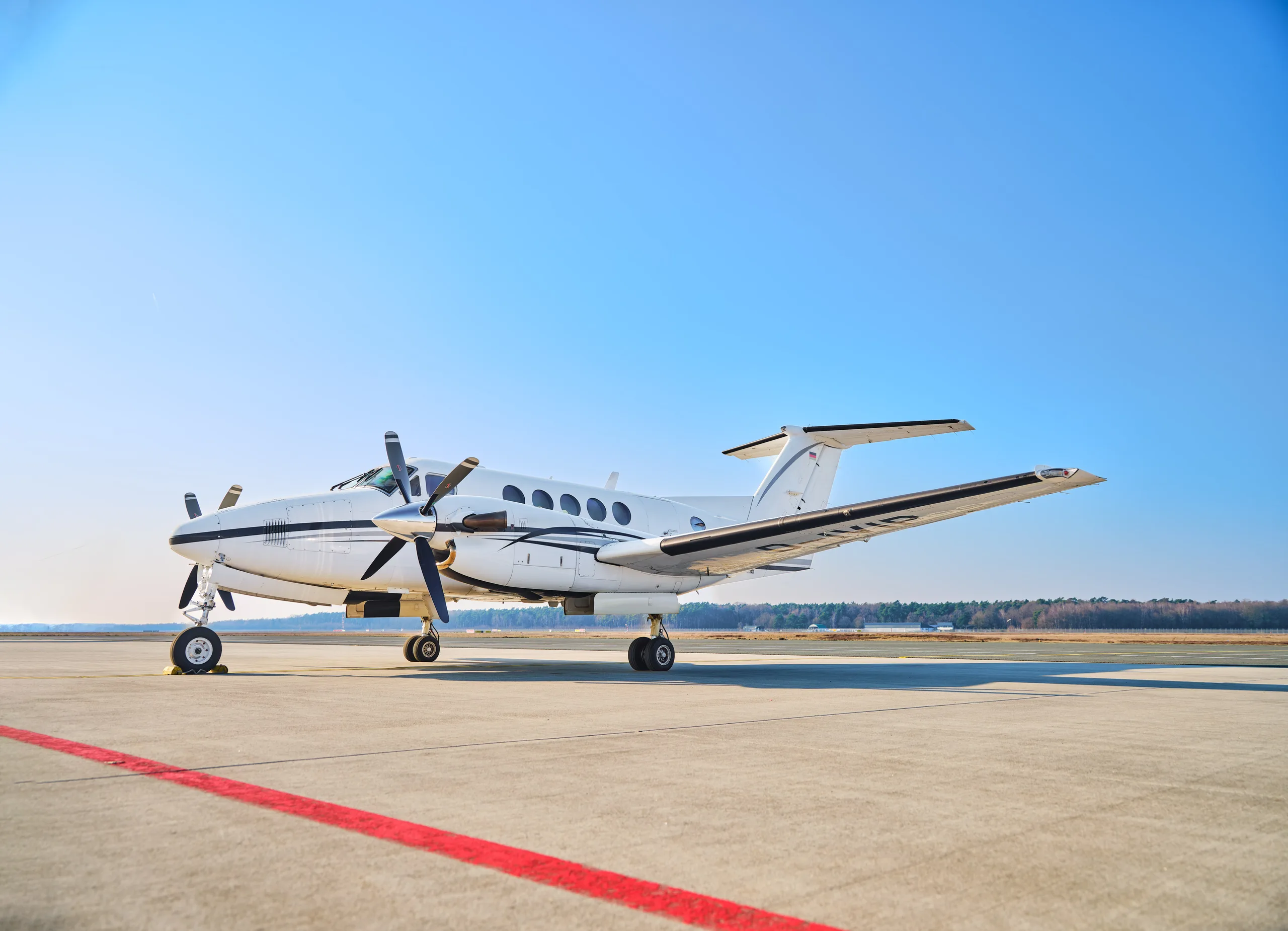 A white and black twin-turboprop aircraft, likely a King Air, is parked on an airfield under a clear blue sky.