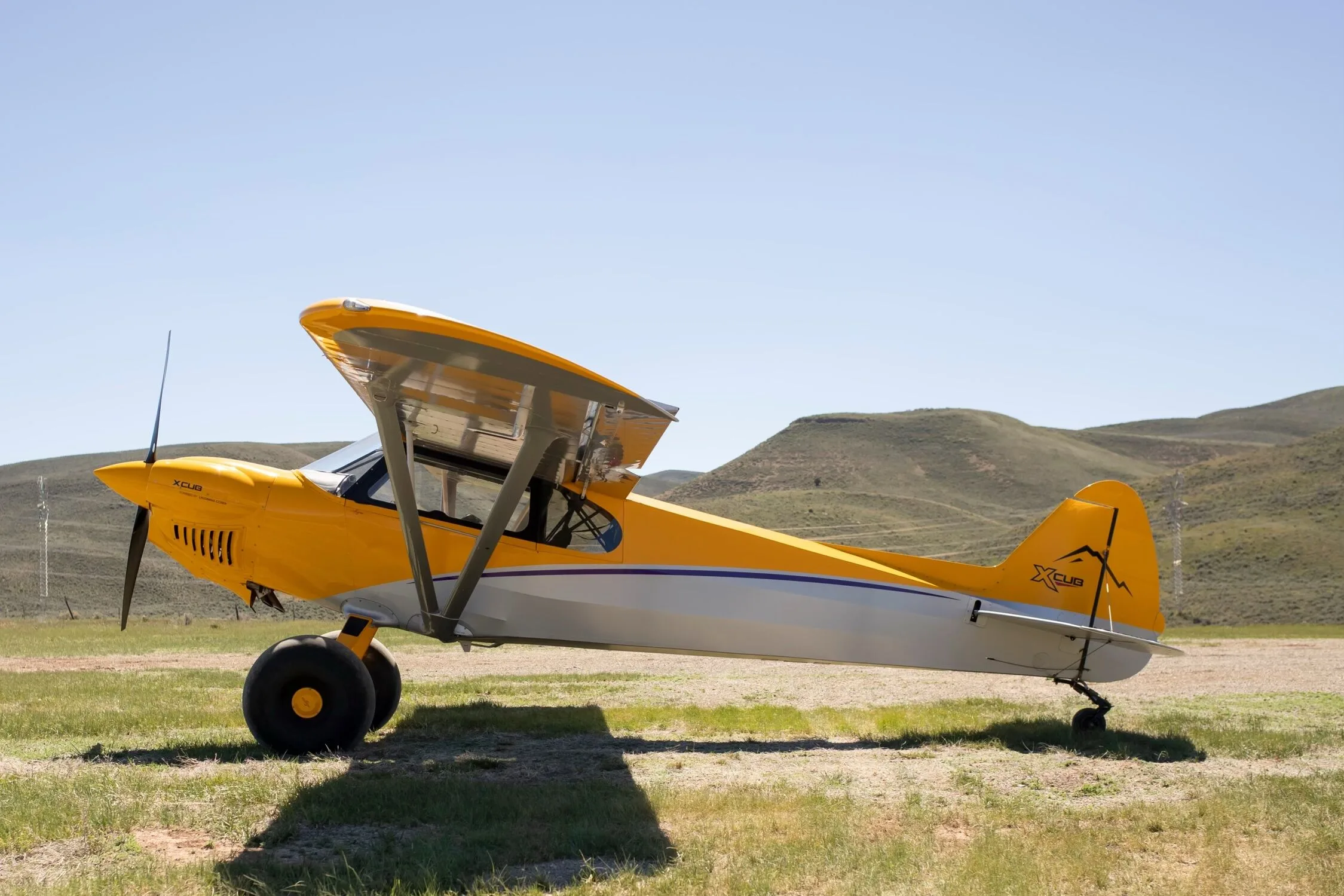 A three-quarter front view of a yellow and silver CubCrafters XCub aircraft with large bush tires on a grassy field.