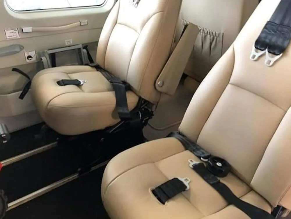 Two tan leather passenger seats with black seatbelts inside the aircraft cabin.