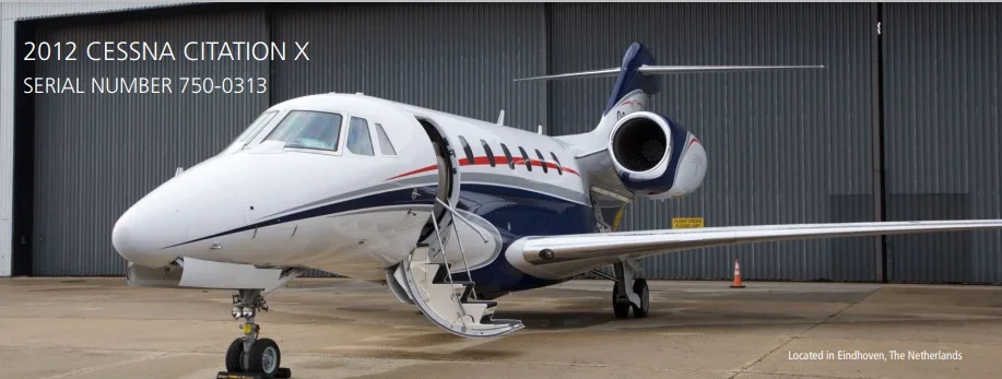 A 2012 Cessna Citation X (serial number 750-0313) with its door open is parked on a tarmac in front of a hangar.