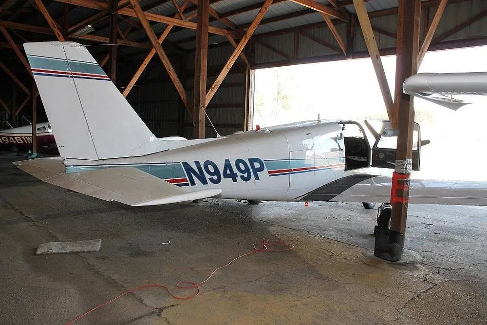 The rear-right side of a white single-engine propeller aircraft, N949P, with blue and red stripes, parked in a hangar.