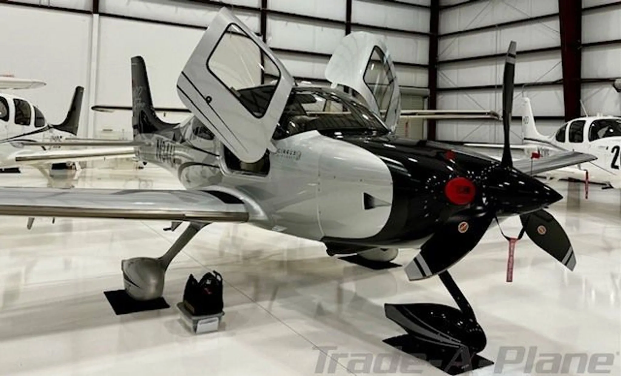 A black and silver Cirrus SR22 GTS Turbo aircraft with open doors is parked in a hangar.