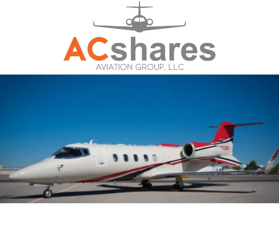 A white private jet with red and black stripes is parked on a tarmac under a clear blue sky, with a company logo above.