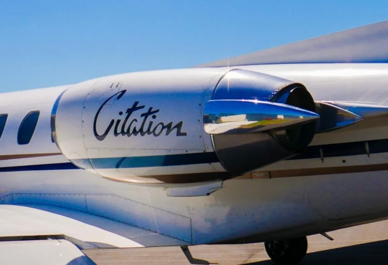 A close-up view of the "Citation" logo on the engine nacelle of a white business jet with blue and gold stripes.