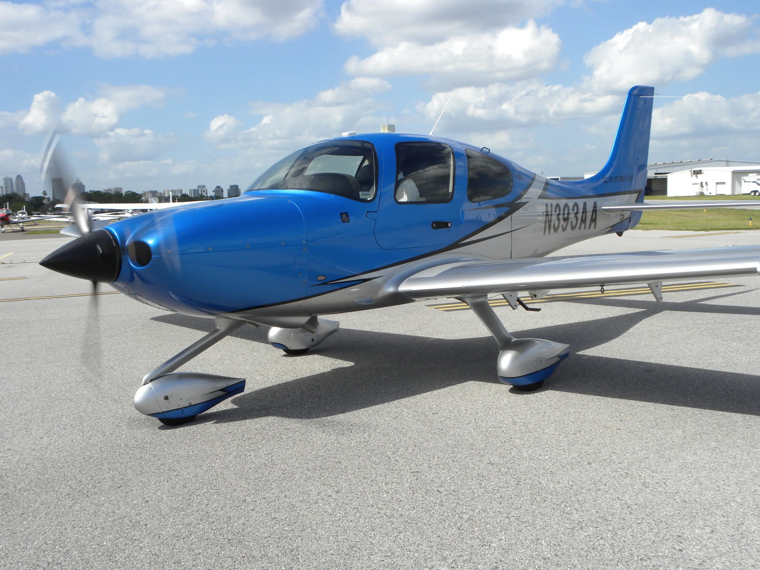 A blue and silver Cirrus SR22 aircraft with registration N393AA, parked on an asphalt ramp.