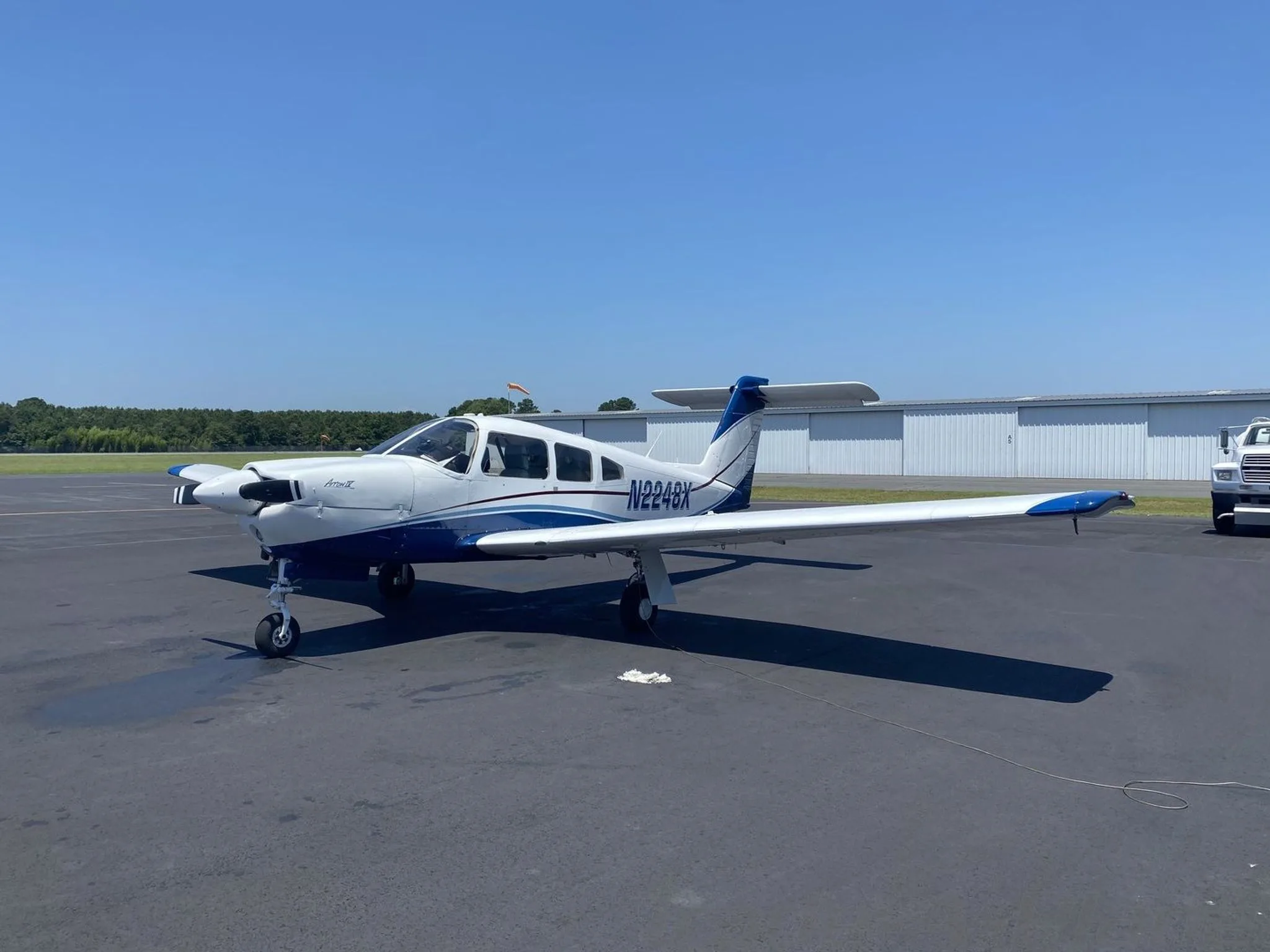 A white and blue Piper Archer II (N2248X) parked on an asphalt ramp under a clear blue sky.