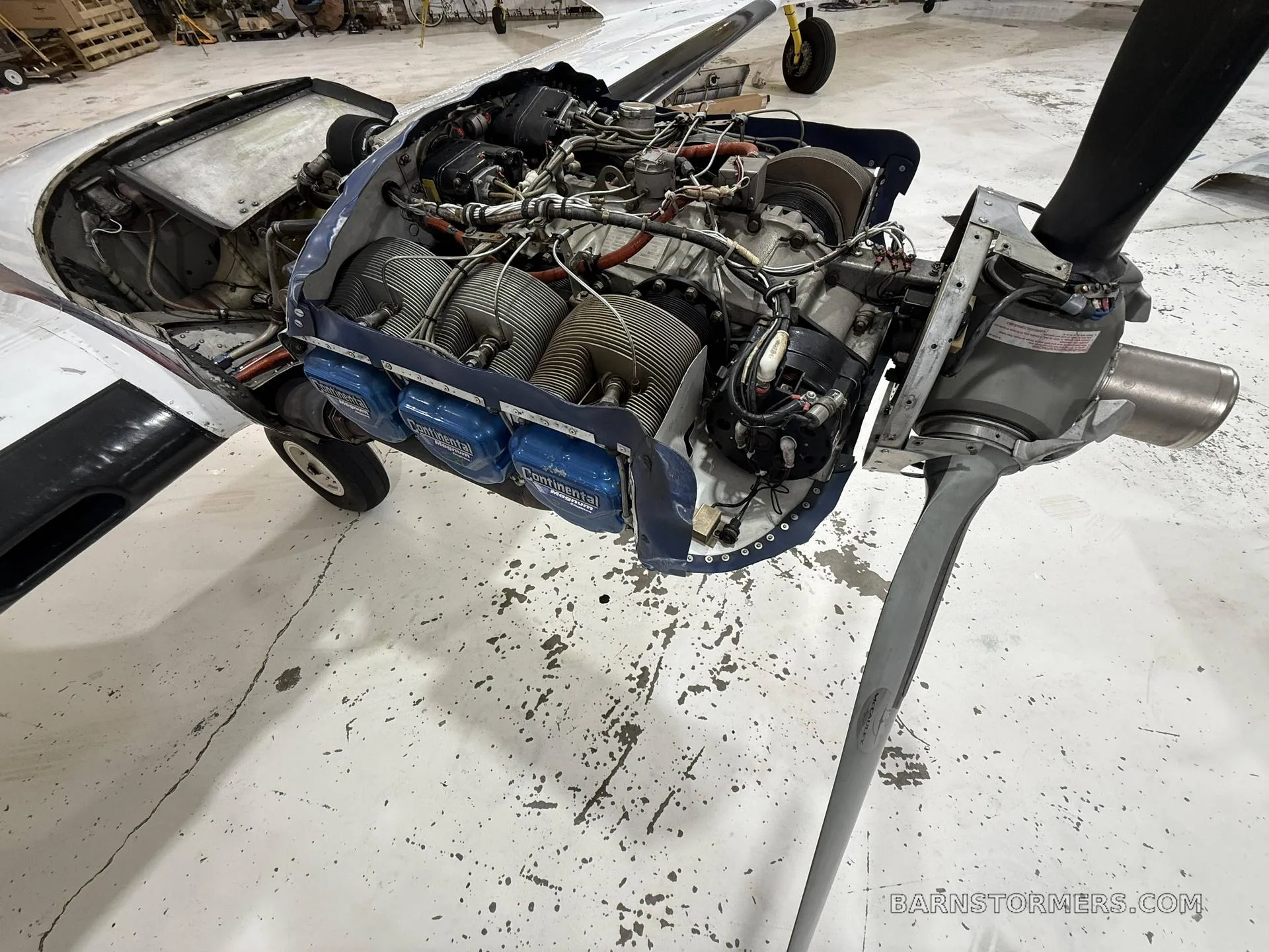 A close-up view of a Continental aircraft engine with its cowling removed, showing cylinders and wiring, in a hangar.