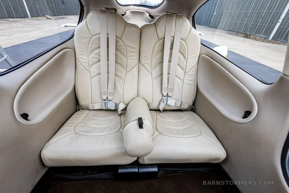 The beige leather rear seats of a Cirrus SR22 aircraft cabin are visible with seatbelts fastened.