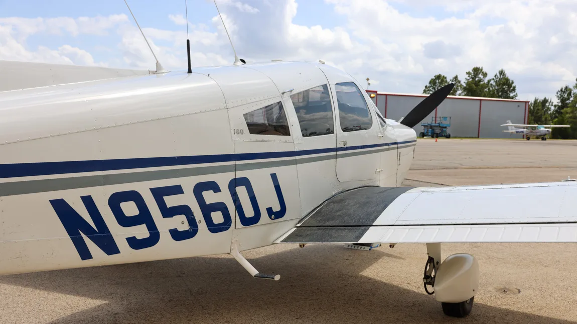 Close-up of the fuselage of the Piper Cherokee 180 (N9560J) showing the registration and wing root.