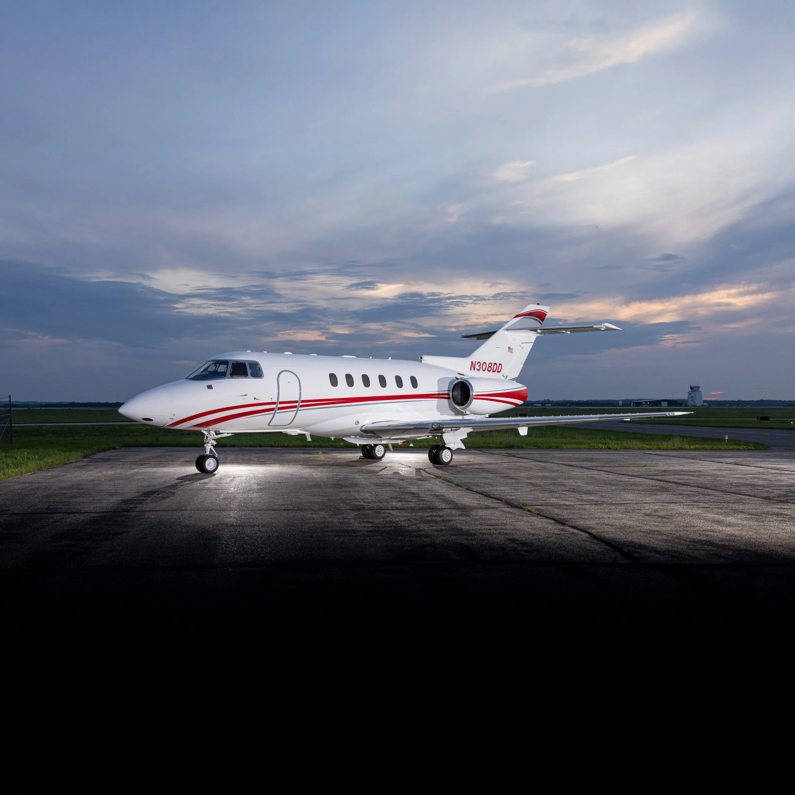 A white business jet with red stripes, registration N308DD, parked on an airfield at dusk.