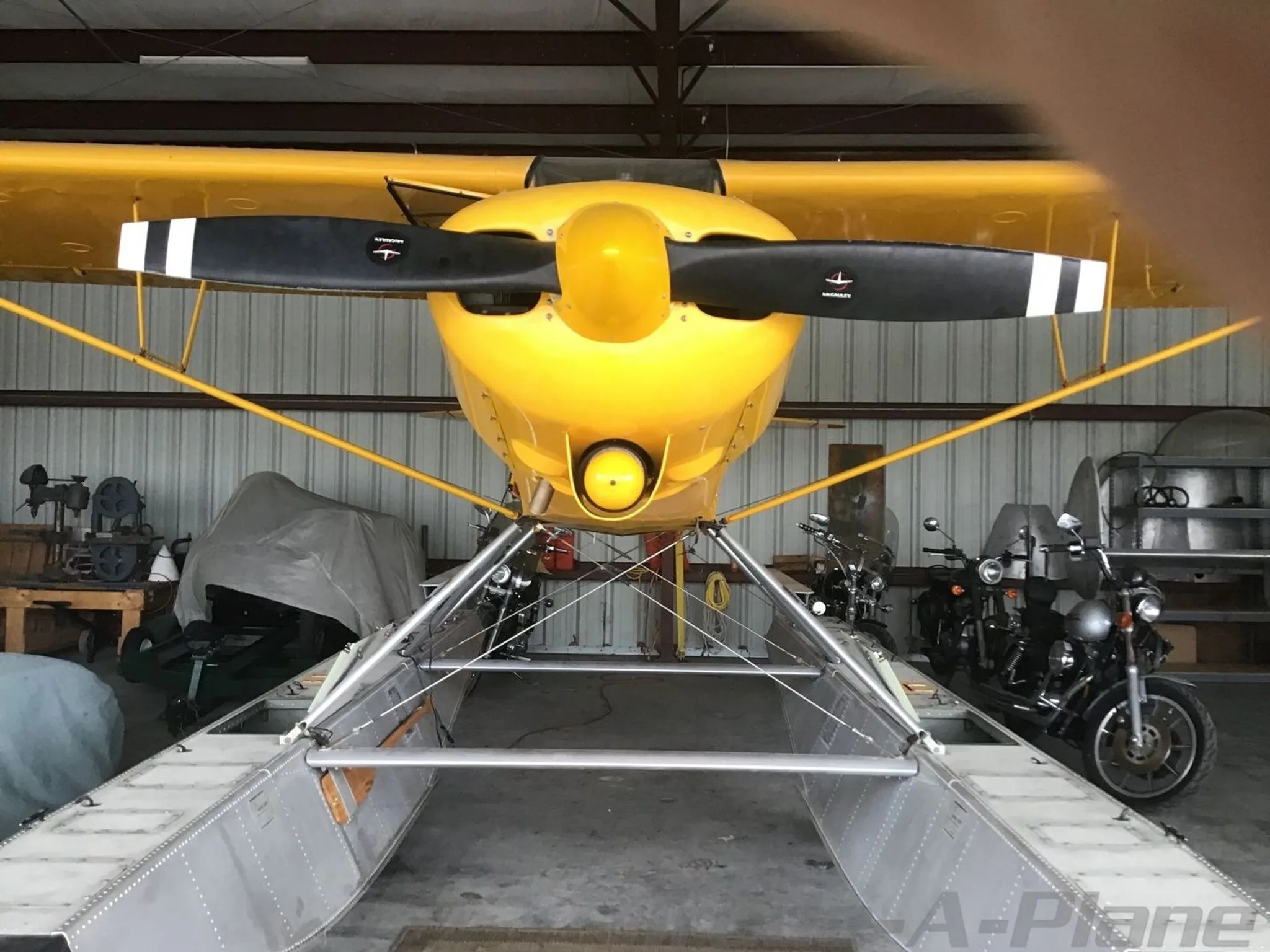 Front view of a yellow Piper Super Cub floatplane (N80AN) with a two-blade propeller, parked in a hangar.