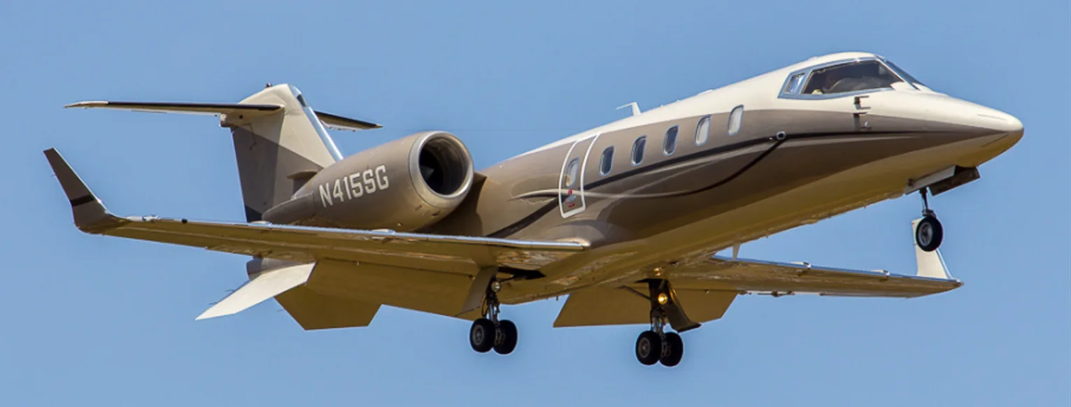 A Learjet 75 aircraft with registration N415SG in a two-tone brown and white paint scheme, flying with landing gear extended against a blue sky.