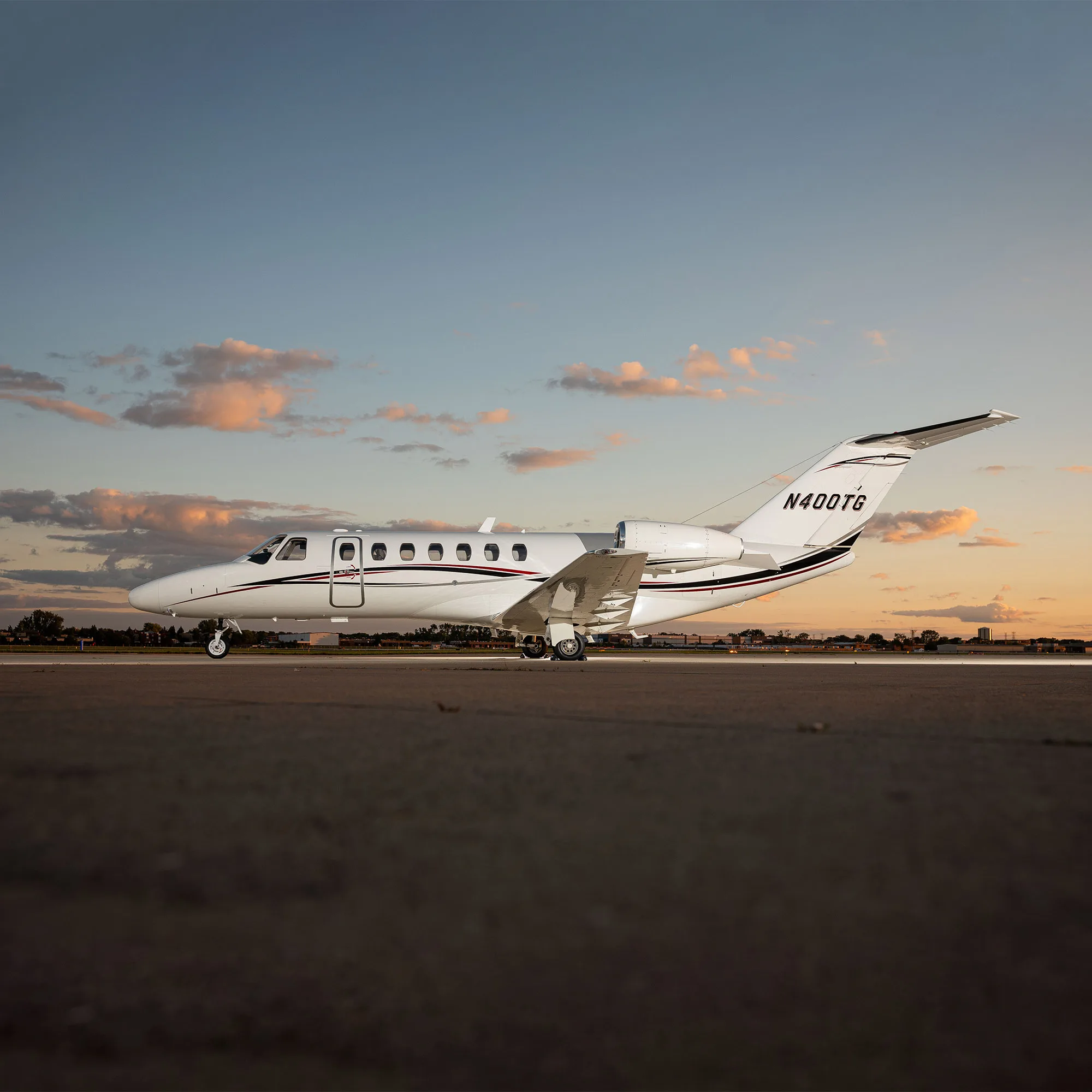 A white business jet with black and red stripes (N400TG) sits on a tarmac at sunset.