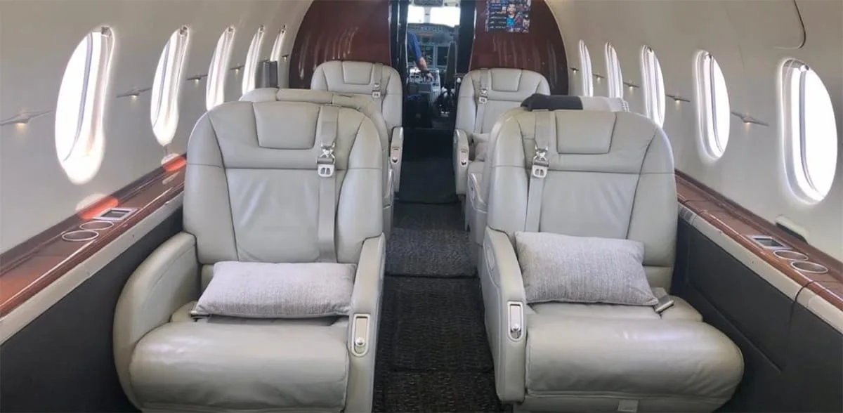 The aircraft's cabin interior features light grey leather seats and wood paneling.