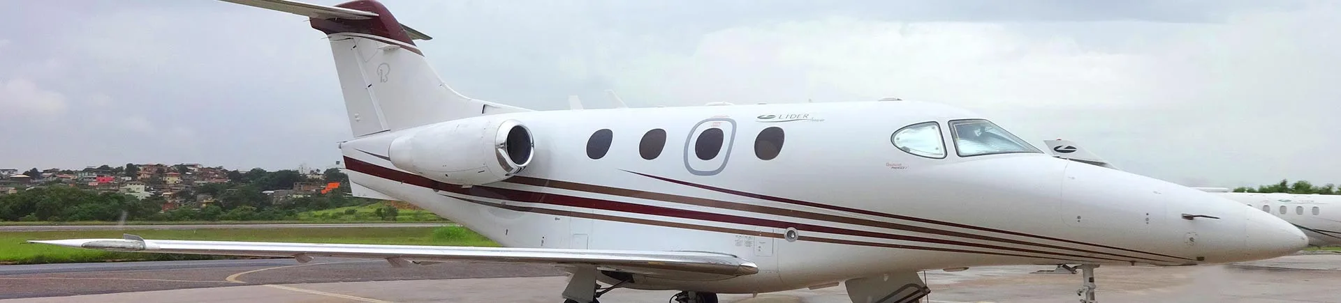 Side view of a white and maroon Embraer Phenom 300 on the tarmac.