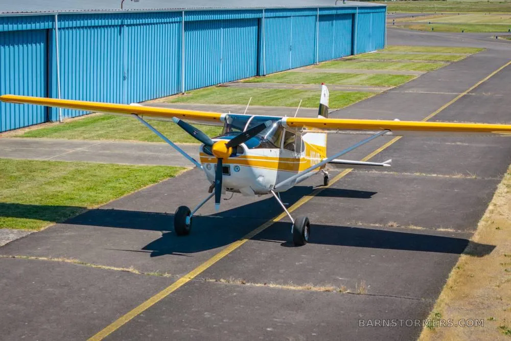A front-quarter view of a white and orange single-engine propeller aircraft with tail number N1841R parked on an asphalt ramp.
