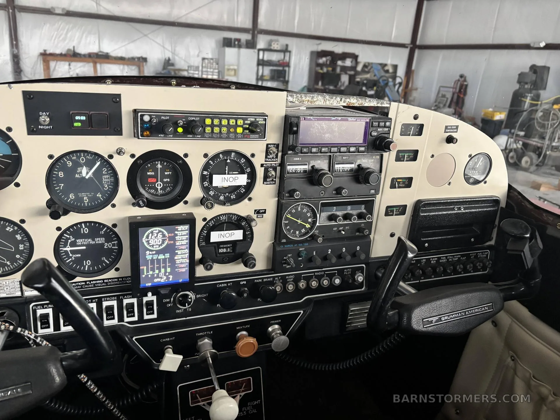 The cockpit instrument panel of a Grumman American aircraft, showing analog gauges, digital displays, and controls.