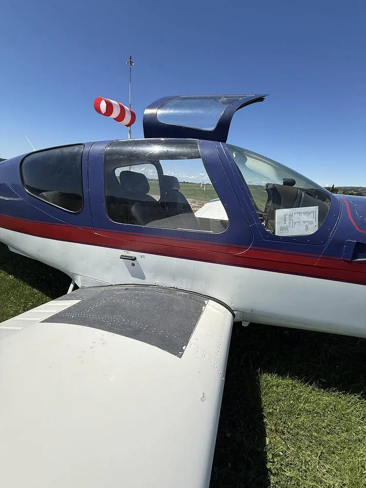 A close-up view of the blue and white Socata Trinidad aircraft with its canopy open, showing the front seats.