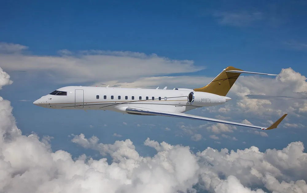 A white business jet with gold tail and winglets, registration N918TA, flying above clouds.