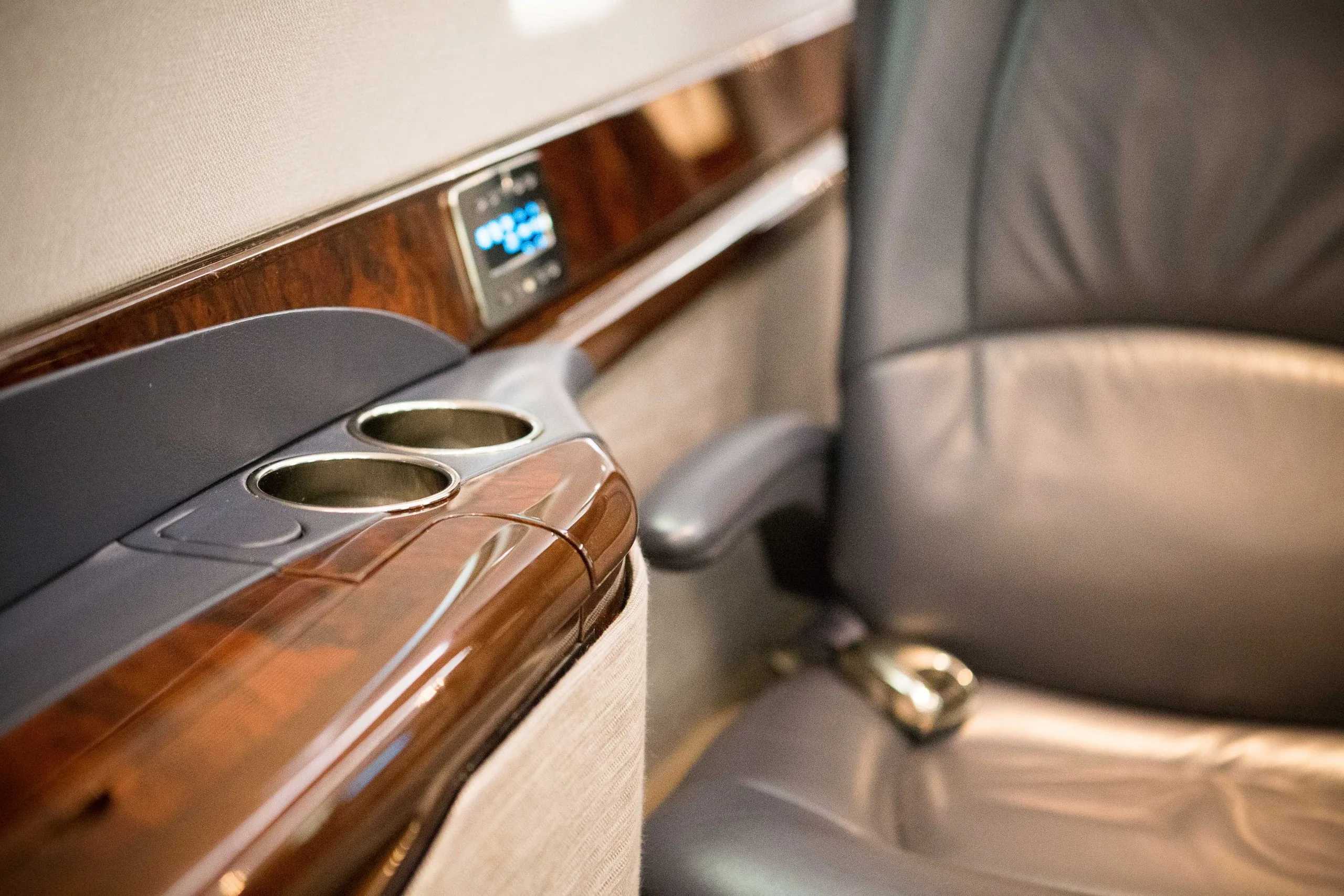 A close-up of the aircraft cabin's leather seat and wood trim with cupholders.