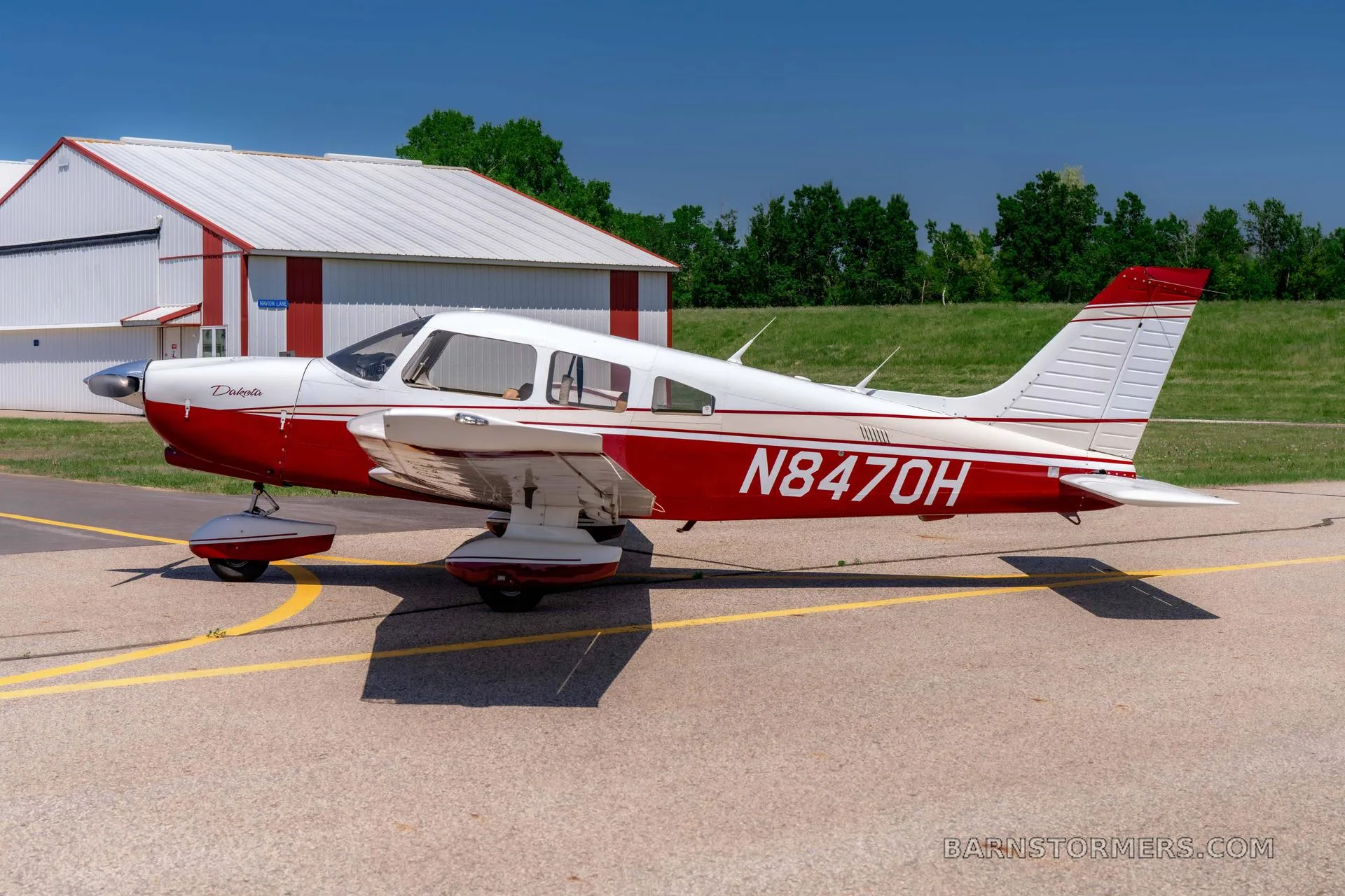 A red and white Piper Dakota aircraft with registration N847OH is parked on an asphalt tarmac in front of a hangar.