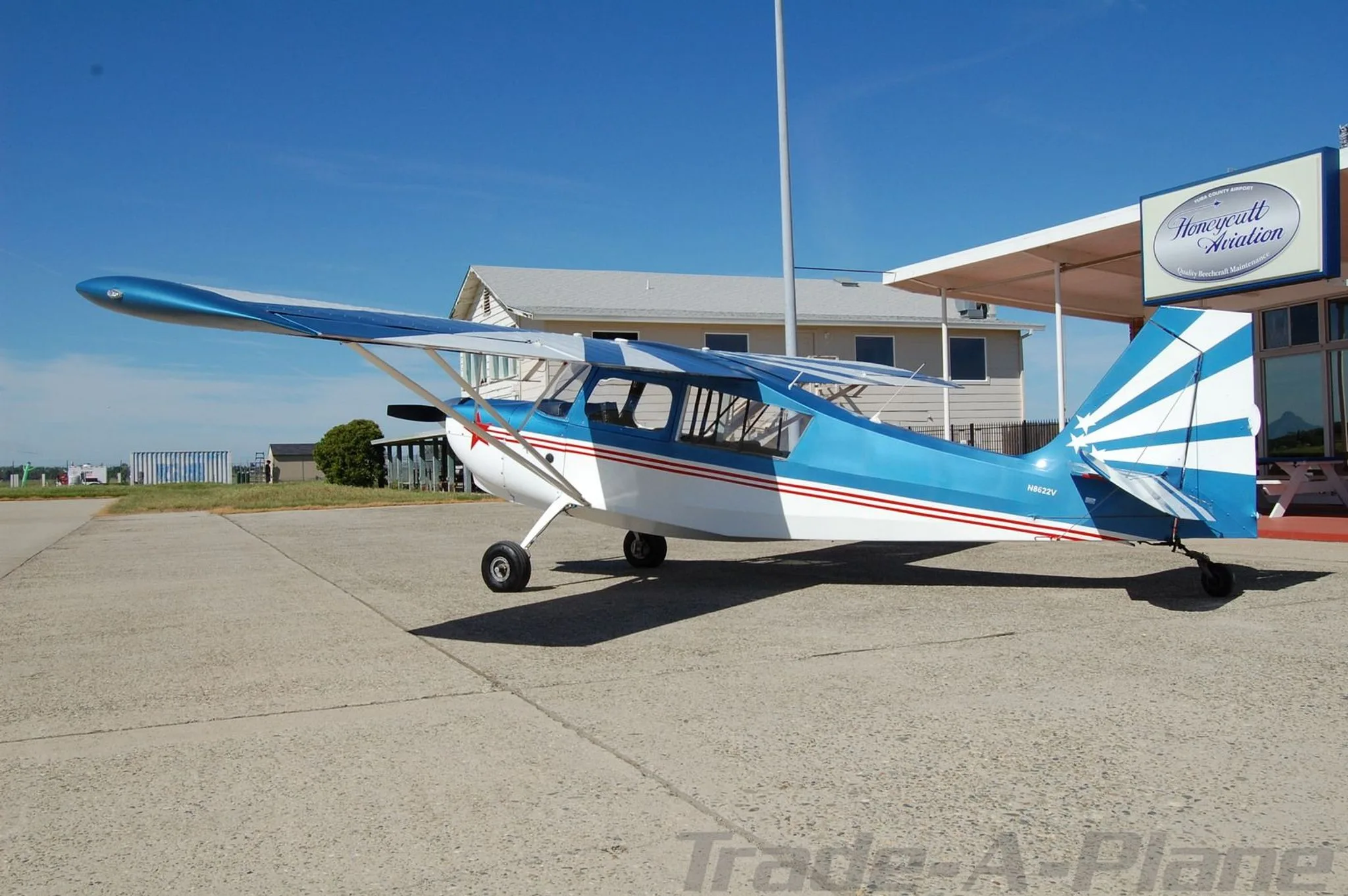 A side view of the blue, white, and red single-engine aircraft with N8622V registration, parked on an airfield with a building in the background.