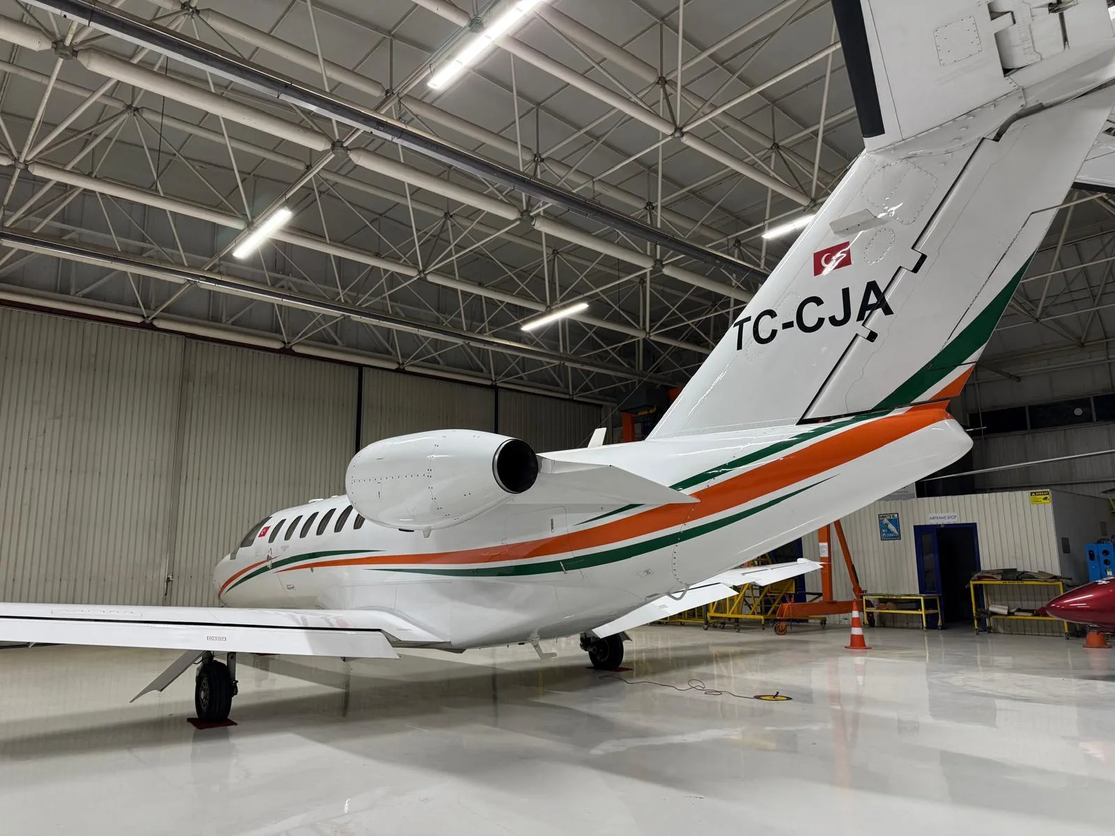 Rear view of a white business jet with orange and green stripes and Turkish flag tail number TC-CJA, parked in a hangar.