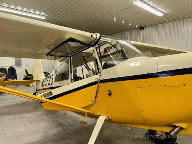 A side view of a yellow and white high-wing aircraft with its doors open, parked inside a hangar.