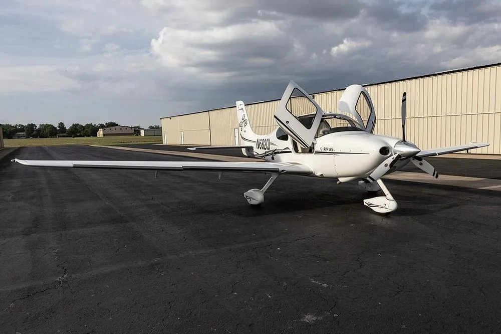 A white Cirrus SR22T aircraft with black and gold accents, registration N682CD, parked on an airfield with its doors open, viewed from the front-right.