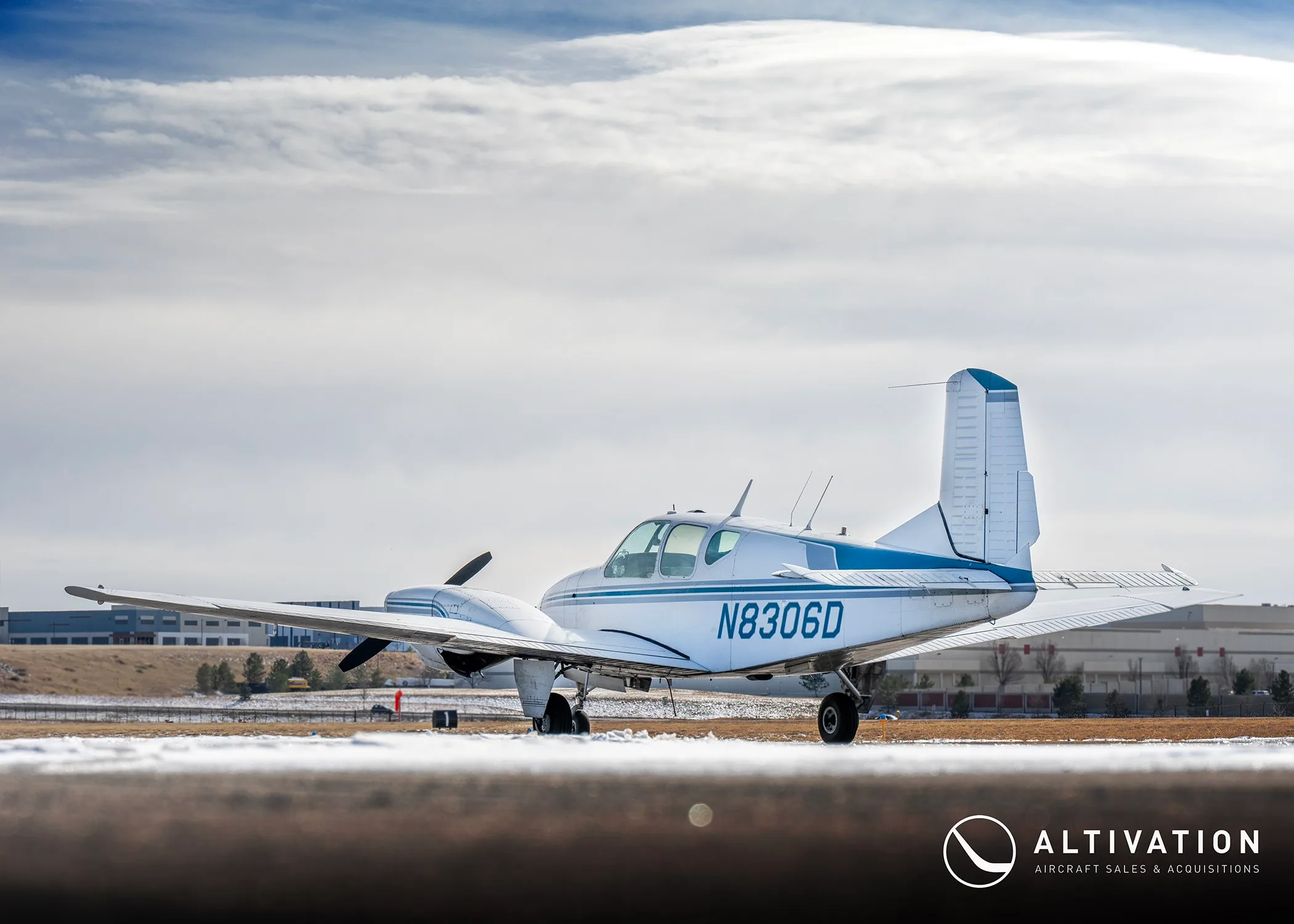 Right side view of a white and blue twin-engine propeller aircraft with registration N8306D on a snowy tarmac.