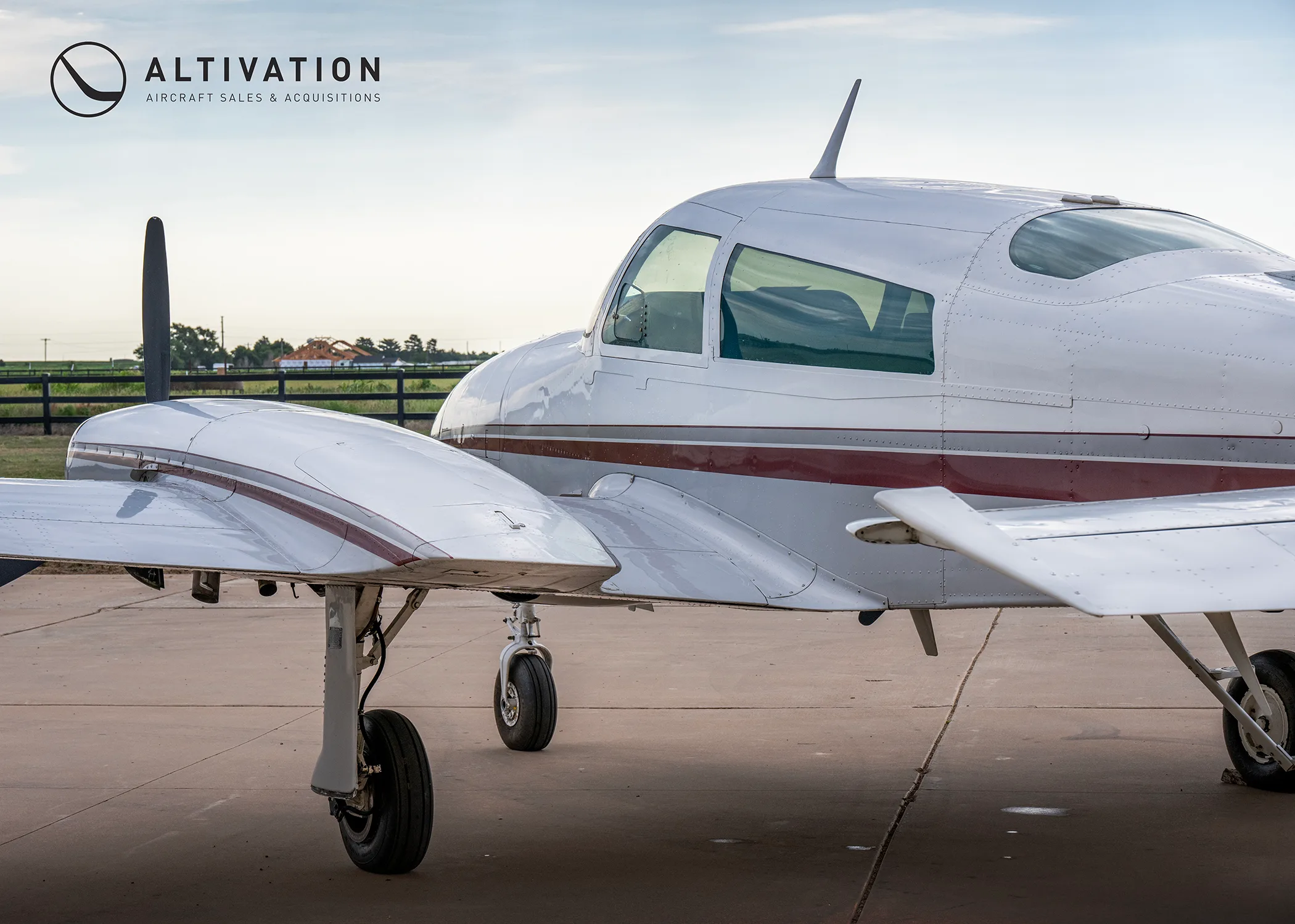 A close-up side view of the fuselage and wing of a white twin-engine propeller aircraft with red and grey stripes.