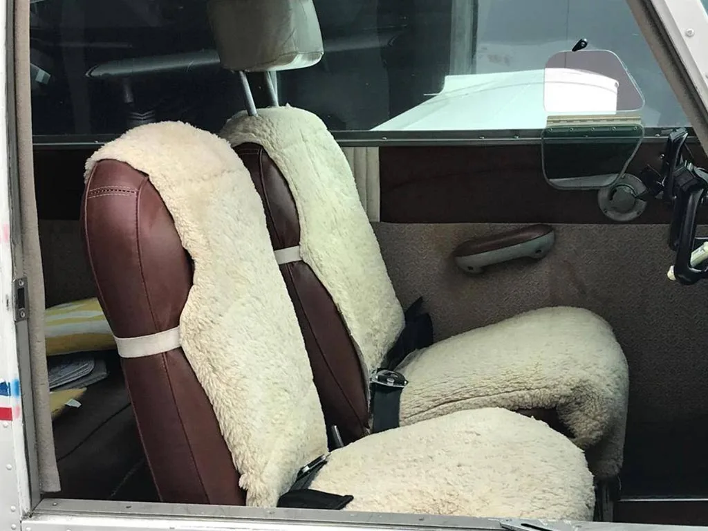The aircraft's interior showing two brown seats with white sheepskin covers.