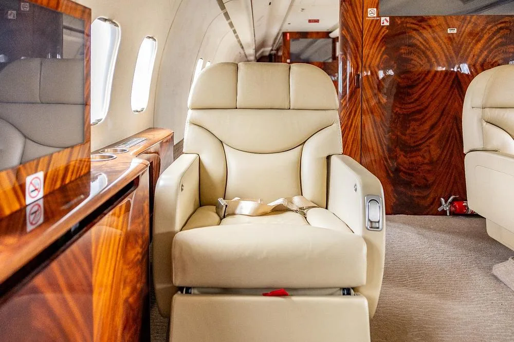 A single cream leather seat with a footrest in a luxurious aircraft cabin.