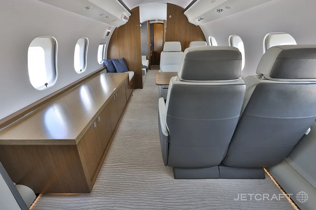 The rear section of the Bombardier Global 6000 cabin, with a long wooden credenza on one side and grey leather seats facing forward.