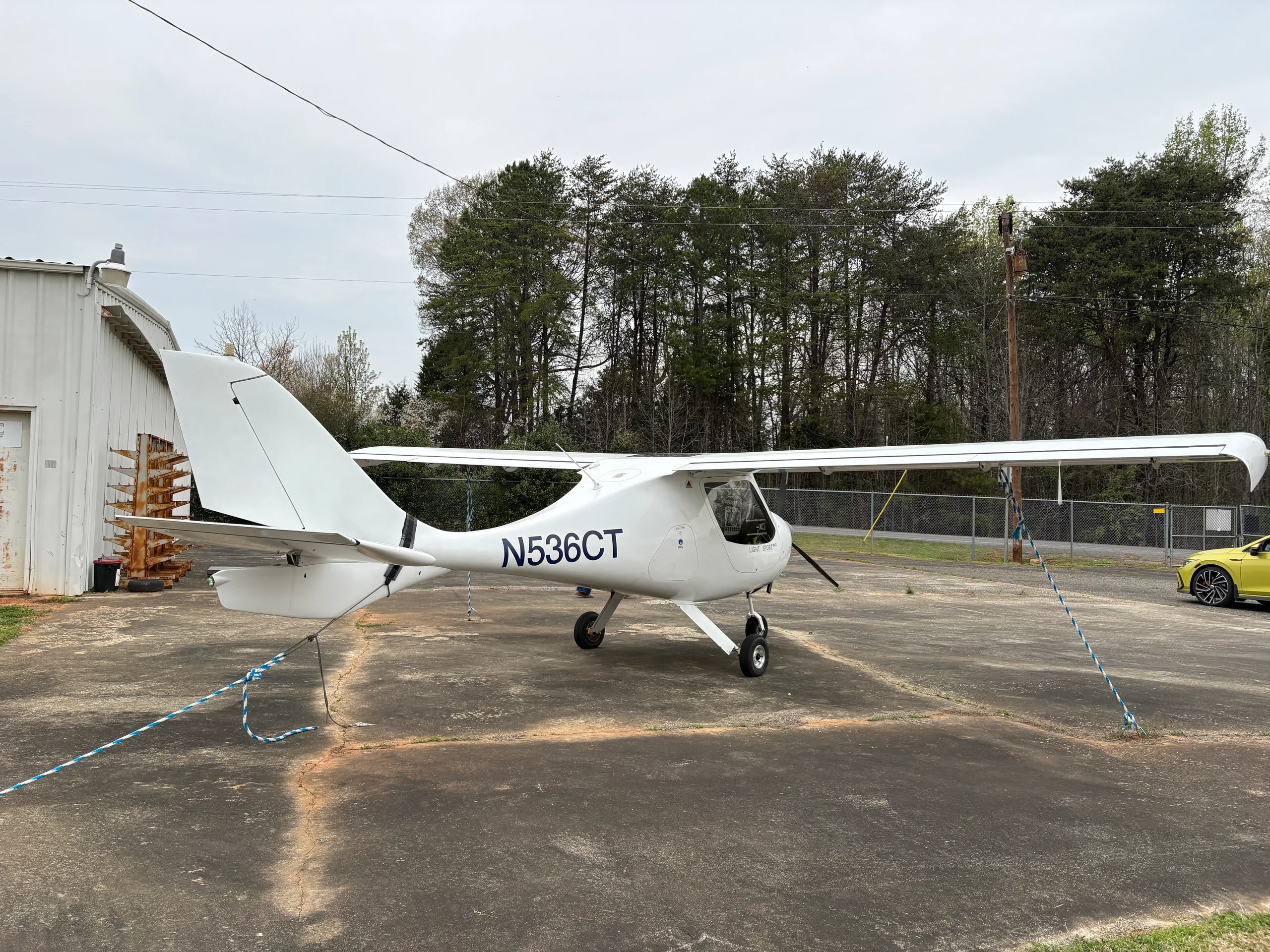 A white light sport aircraft, N536CT, is parked on a tarmac with trees and a fence in the background.